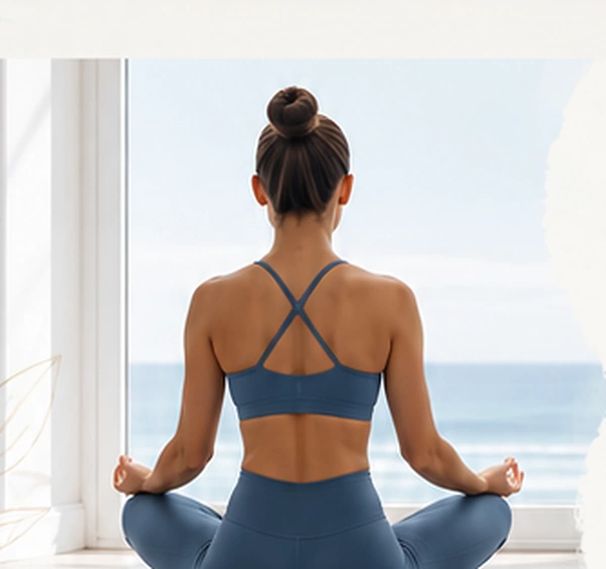 Mujer de espaldas meditando en postura de loto frente a una ventana con vista al mar